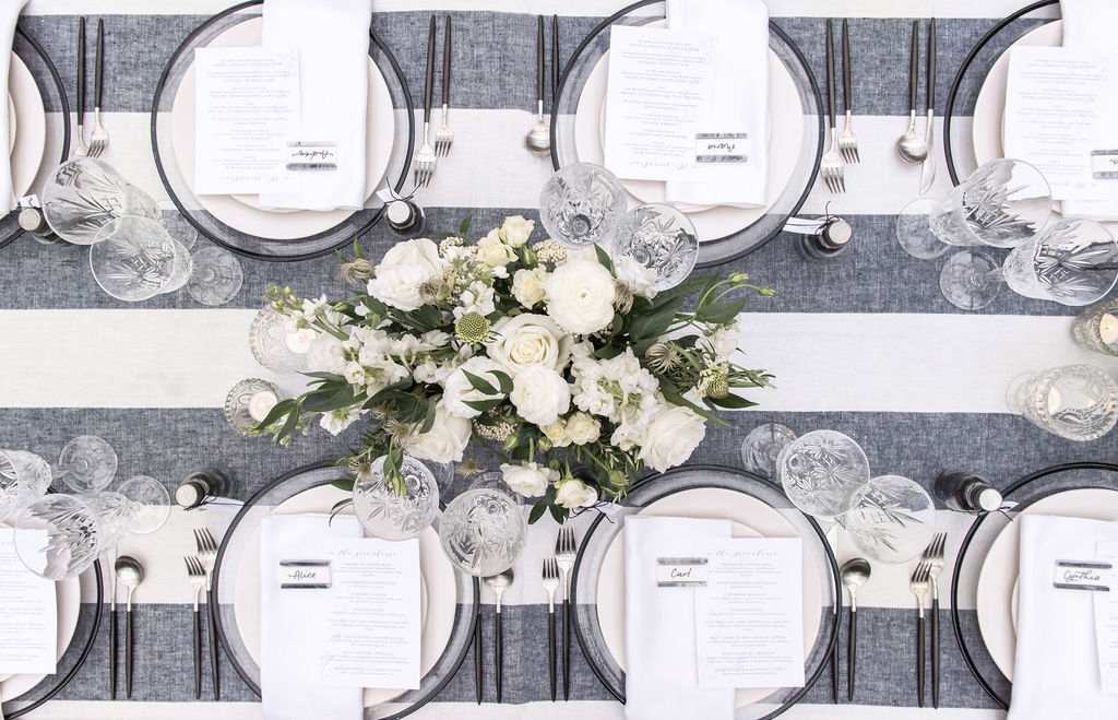 Table set with blue and white striped linen, white napkins and white floral arrangements