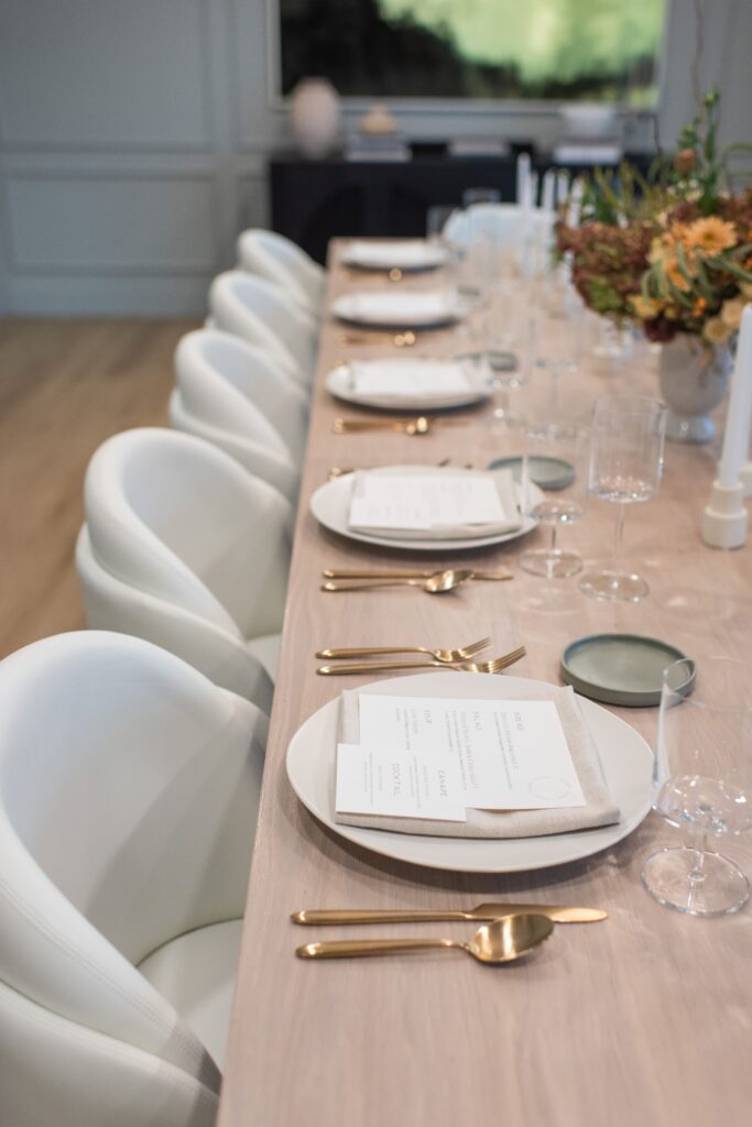 Wood table with wood plates, gold cutlery and white chairs