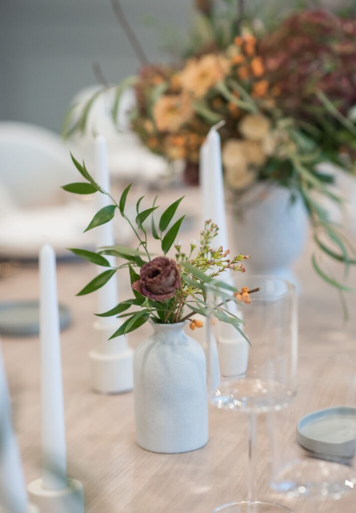 White ceramic vase with burgundy rose and greenery